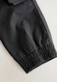 Black pant cuff featuring a gathered elastic waistband and smooth texture, with a subtle sheen and minimalist design.