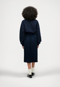 Ναυ�τικό φούτερ με χαμηλούς ώμους σε συνδυασμό με πλισέ ναυτικό φούστα και μαύρα παπούτσια. Λευκές κάλτσες είναι ορατές πάνω από τα παπούτσια.