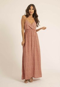 Robe maxi en rouille avec un motif de pois blancs. Elle présente un corsage torsadé, des bretelles réglables et une jupe fluide. Portée avec des sandales à lanières.