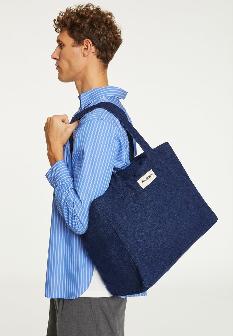 Sac fourre-tout navy en matériau feutré avec deux poignées, de forme rectangulaire et une étiquette latérale. Présente une surface texturée.