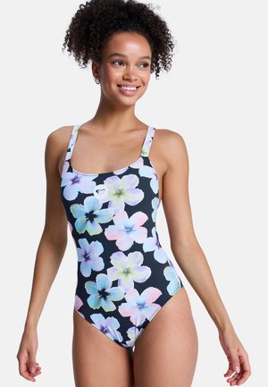 Junge Frau lächelnd, trägt einen schwarzen Badeanzug mit großen Pastellblumenmustern und dünnen Trägern.