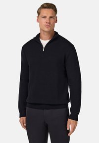 Dzianinowy ciemnoniebieski pulower z kieszenią na ćwierć zamka, strukturalnym wzorem oraz ribbowe wykończenia przy hemie i mankietach, zestawiony z dopasowanymi ciemnymi spodniami.