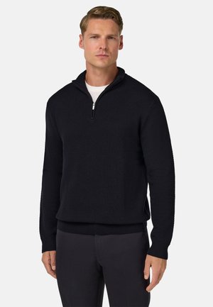 Gebreide donkerblauwe pullover met een kwart-rits kraag, textuurpatroon, geribbelde zoom en mouwen, gecombineerd met op maat gemaakte donkere broeken.