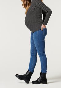 Graviditetstopp med svart och vit horisontell rand, i kombination med blå skinny jeans och svarta snörstövlar med kraftiga sålar.