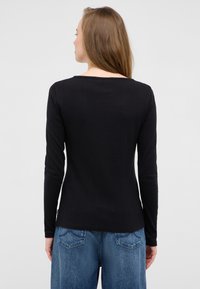 Schwarz gerippte Langarmbluse mit einem weiteren Halsausschnitt. Glatte Textur, taillierter Stil, kombiniert mit hellblauen, weiten Jeans.