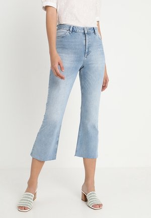 Light blue cropped jeans with a high waist, featuring a relaxed fit and frayed hem. Paired with white open-toe heeled mules.