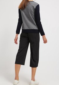 Marinfärgad långärmad topp med mönstrad baksida och enfärgade ärmar, ihop med avklippta svarta byxor med vita vertikala ränder. Vita sneakers.