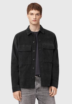 Black corduroy overshirt with two front pockets, button closure, and a structured collar. Soft texture and relaxed fit.