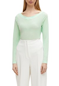 Maglia a maniche lunghe color menta chiaro con scollatura a V, texture morbida e design aderente, abbinata a pantaloni bianchi a vita alta.