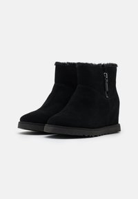Bottines compensées en daim noir avec une fermeture éclair sur le côté et une doublure en fourrure douce au sommet. Texture lisse et semelle extérieure en caoutchouc durable.