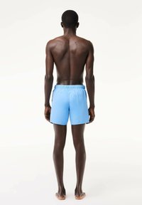 Niebieskie kąpielówki z elastycznym pasem, o gładkiej fakturze i prostym wzorze, widok z tyłu.