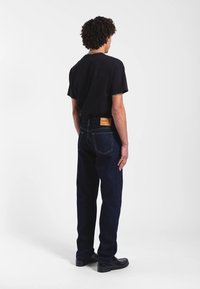 Musta lyhythihainen paita, tummansiniset farkut ja mustat kengät. Farkuissa on nahkainen tunniste takana ja klassinen suora lahkeen malli.