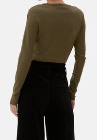 Maglia a maniche lunghe verde oliva con scollatura rotonda, abbinata a pantaloni neri in corduroy a vita alta con tasche laterali e tessuto testurizzato.