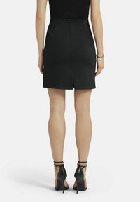 Zwarte kokerrok met een slim fit, voorzien van een achteropening, een gladde textuur en een verborgen ritssluiting in het midden van de achterkant. Gecombineerd met zwarte hoge hakken.