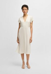 Abito midi crema con scollo a V e maniche corte a campana, caratterizzato da una vita aderente e una gonna fluida. Abbinato a sandali con cinturini.