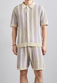 Gebreid kort mouw vest en korte broek set in crème met verticale strepen in lavendel en paars, voorzien van knopen aan de voorkant en geribbelde accenten.