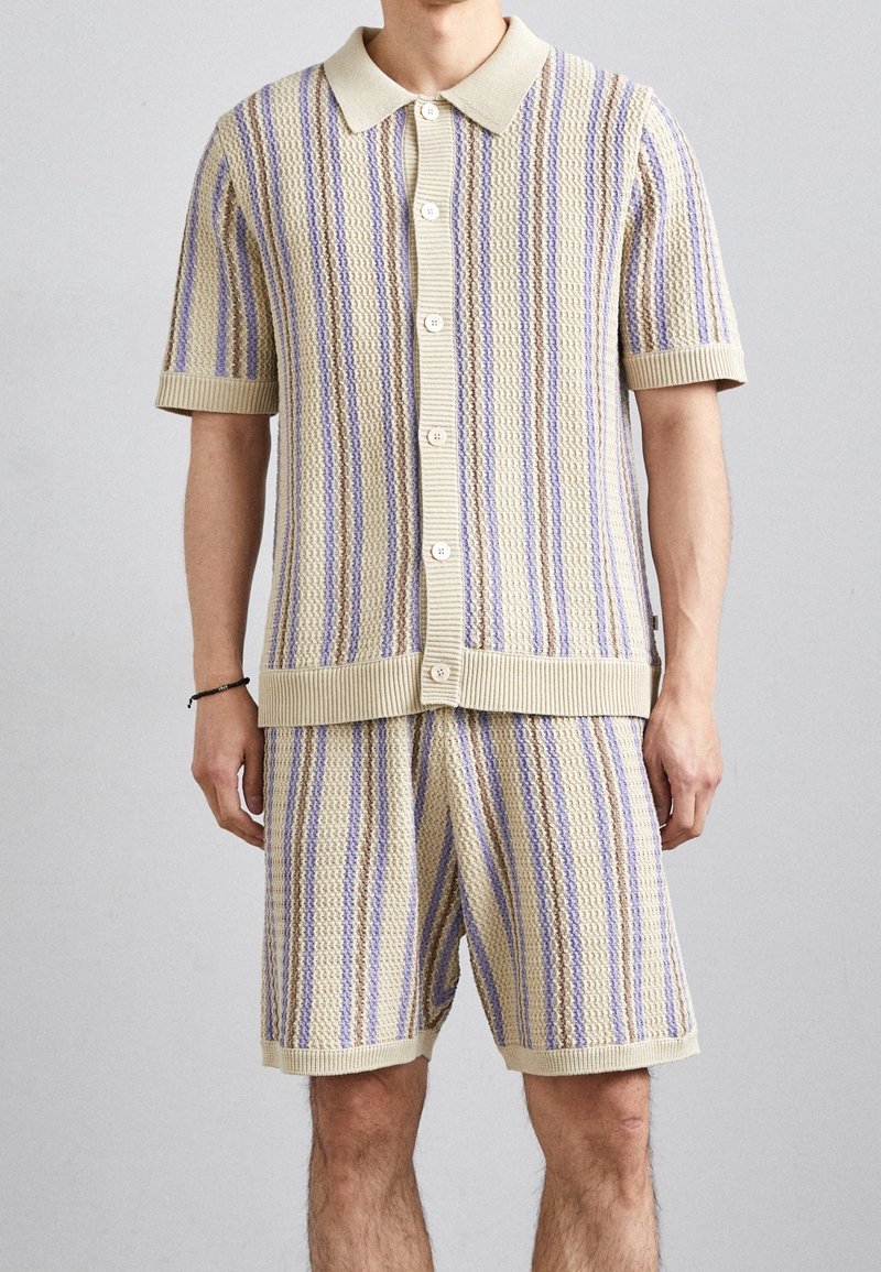 Gebreid kort mouw vest en korte broek set in crème met verticale strepen in lavendel en paars, voorzien van knopen aan de voorkant en geribbelde accenten.