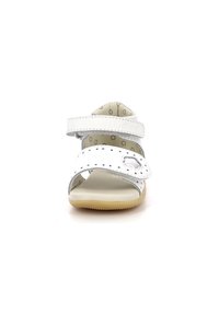 Sandalia de cuero blanca con detalles perforados, correas ajustables, una abertura redonda y una suela de goma flexible. El interior presenta un patrón de puntos.