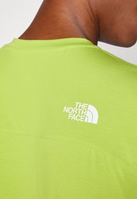 Zielona koszulka z krótkim rękawem i okrągłym dekoltem. Na plecach znajduje się białe logo "The North Face". Gładka struktura, casualowy design.