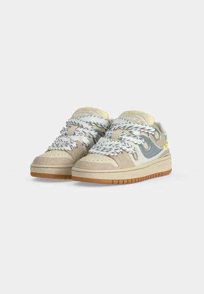Ζεύγος μπεζ και γκρι sneakers χαμηλού τύπου με χονδρά λευκά και γκρι κορδόνια με σχέδιο και ανοιχτό καφέ σόλες σε λευκό φόντο.