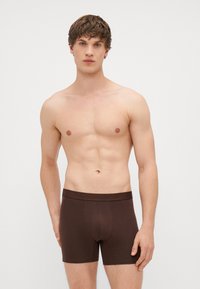 Pruunist puuvillast bokserpüksid pehme vöökoha, sobiva disaini ja siledast tekstuurist, kannab mehes mudel, kellel on sportlik kehaehitus.