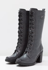 Černé vysoké boty až ke kolenům vyrobené z umělé kůže. Disponují přední šněrováním, kovovými oky a texturovaným blokem na podpatku. Celkově hladký povrch.