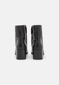 Stivaletti neri con zip, in pelle texture, dotati di tacco spesso e punta arrotondata liscia.