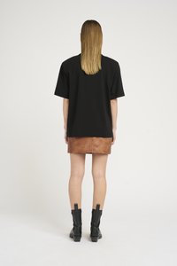 T-shirt nera oversize con maniche corte, abbinata a una mini gonna in pelle marrone. Il modello indossa stivali neri alla caviglia con finitura texturizzata.