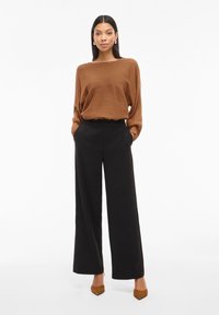 Pull oversized à rayures marron associé à un pantalon large noir taille haute et des escarpins bruns à bout pointu. Design simple et épuré.