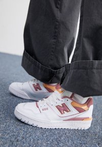 Baskets New Balance 550 blanches avec des accents roses et oranges. Design en cuir perforé avec une semelle texturée et logo de marque sur le côté.
