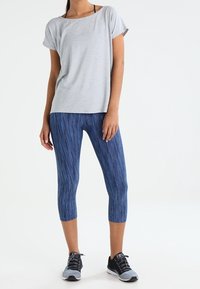 Gray short-sleeve T-shirt paired with blue patterned leggings, featuring a fitted design and ankle length, complemented by black athletic shoes.