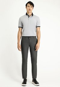 Grijze polo met zwarte kraag en manchetten, gecombineerd met donkergrijze op maat gemaakte broek en zwarte sneakers, gepresenteerd op een neutrale achtergrond.