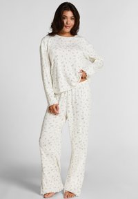 Crème-kleurige pyjama set met een langslavige top en losse broek, beide met een subtiel bloempatroon en geribbelde textuur.
