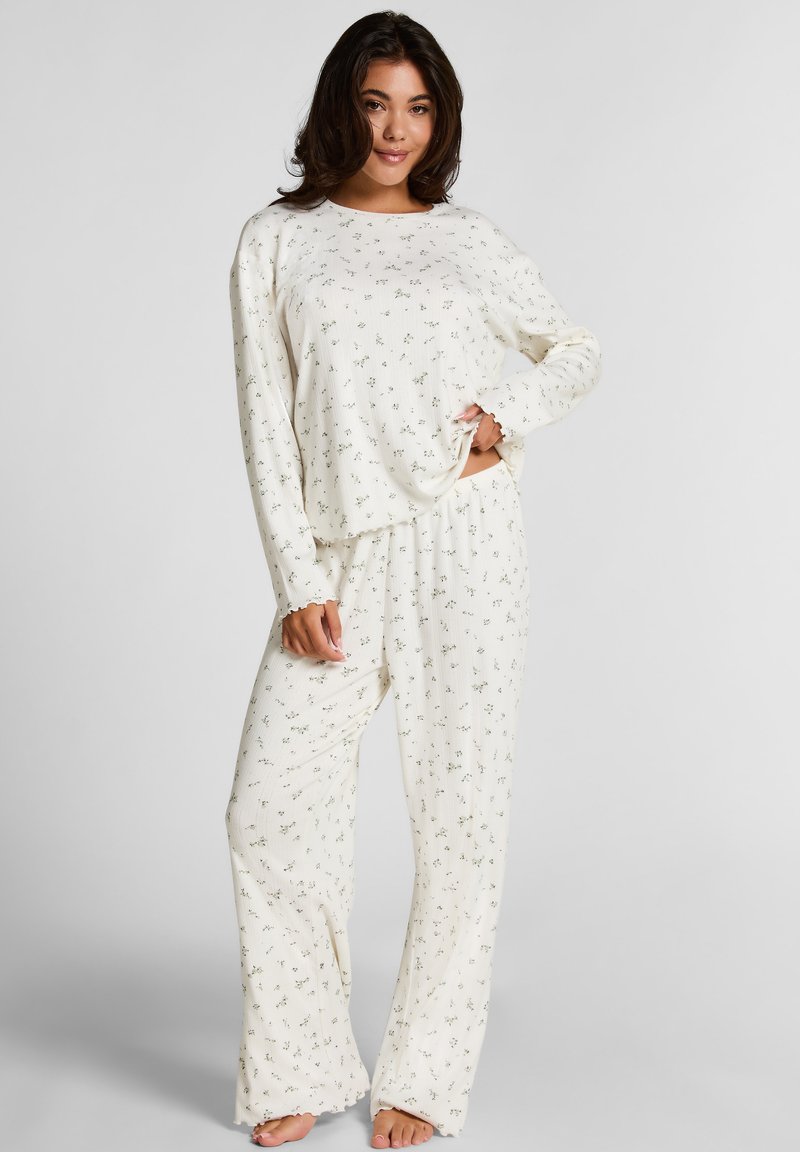 Crème-kleurige pyjama set met een langslavige top en losse broek, beide met een subtiel bloempatroon en geribbelde textuur.