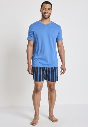 Blue short-sleeve V-neck T-shirt paired with navy shorts featuring vertical blue stripes. Model stands barefoot against a neutral background.
