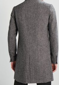 Cappotto in lana grigio a spina di pesce con vestibilità su misura, apertura singola e polsini abbottonati. Texture liscia con motivo distintivo e silhouette moderna.