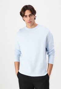 Light blue knit sweater with a round neckline, long sleeves, and ribbed cuffs. The fabric appears soft and smooth, suitable for casual wear.