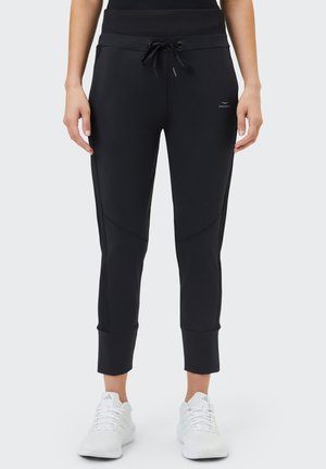 Schwarze Sporthose mit Kordelzugbund, geripptem Bund, schmal zulaufenden Beinen und dezenten Nahtakzenten, kombiniert mit weißen Turnschuhen.