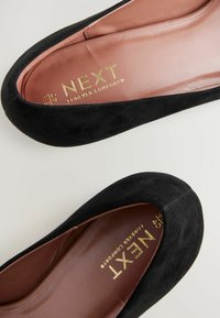 Fekete velúr balettcipők, lekerekített orral és sima bézs talppal. Az insole-on aranyszínű „NEXT Forever Comfort” logó van debütálva.