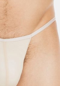 Beige Stringunterwäsche mit dünnen Trägern, weichem Textur und minimaler Bedeckung. Sichtbare Nahtdetails an den Seiten.