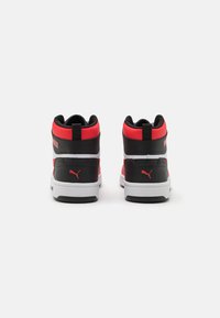 Sneakers typu high-top z czarnej skóry i czerwonymi akcentami wykonanymi z syntetyku. Biała podeszwa z detalem logo, teksturowany tył i wyprofilowany kołnierz dla wsparcia.