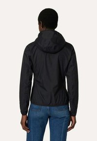 Svart lättviktsjacka med huva, har en slät yta, elastiska ärmmuddar och en figurnära design, som bärs med blåjeans.