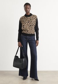 Svetr s leopardím vzorem v béžové a černé barvě, zkombinovaný s tmavými rozšířenými džíny. Modelka drží černou koženou kabelku přes rameno.