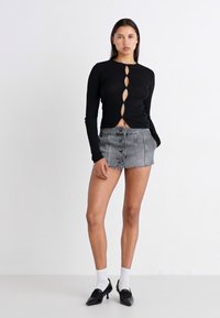 Haut noir à manches longues avec des découpes boutonnées, associé à un short en denim gris taille haute doté de boutons à l'avant et d'un ourlet effiloché.