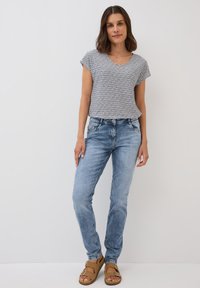 Randig kortärmad skjorta, ljusblå jeans, beige sandaler. Skjortan har rund halsringning; jeansen har framfickor och lätt slitningar.