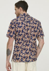 Korte mouwen shirt in marineblauw met een bloemenpatroon met oranje en crèmekleurige botanicals. Lichtgewicht stof met een ontspannen pasvorm.