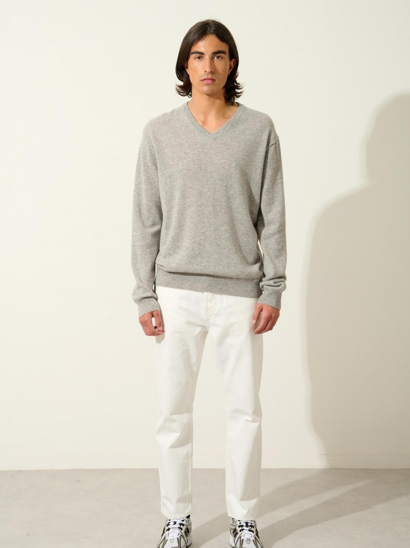 Grå v-ringad tröja med lång ärm, parat med vita jeans och mönstrade sneakers. Slät textur med en avslappnad passform.