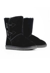 Botas de ante negro con punta redonda, suela de goma plana y acentos de botones laterales con recortes triangulares. Forro interior suave visible.
