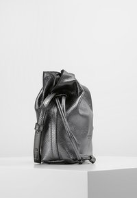 Borsa a sacco in pelle grigia metallica con superficie testurizzata, dotata di due cinghie regolabili e chiusura superiore arricciata.