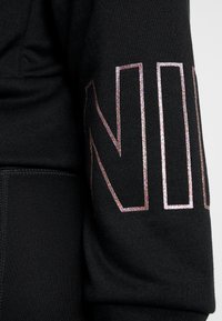 Svart sweatshirt med en glänsande, iriserande "NIV"-tryck på ärmen. Mjuk textur med ribbat ärmslut. Avslappnad passform.